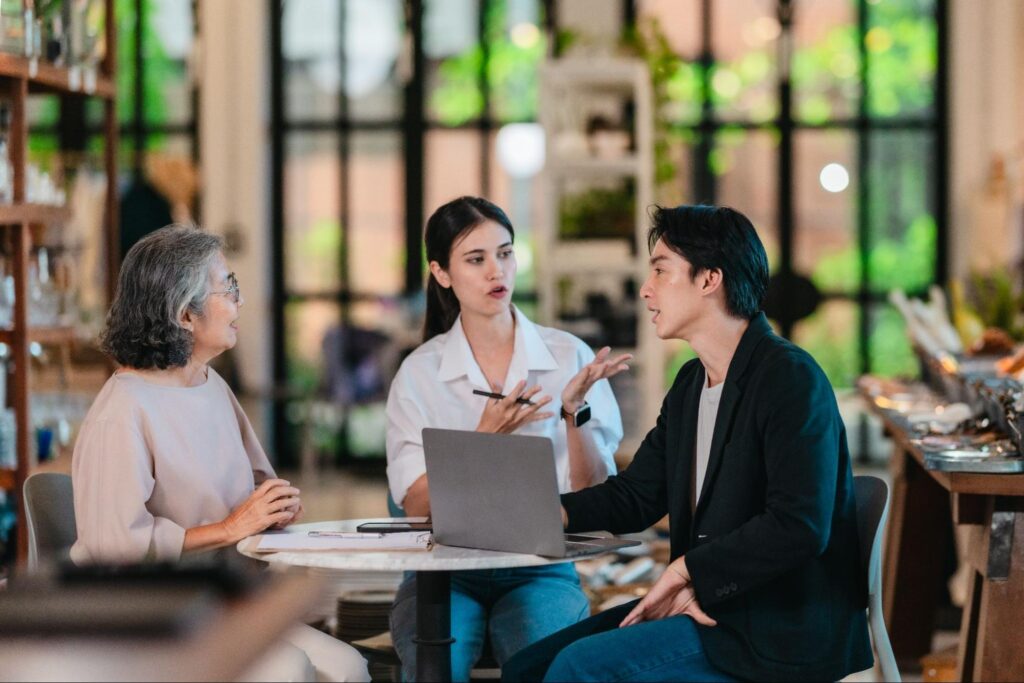 Three people discussing plans at a café table with a laptop