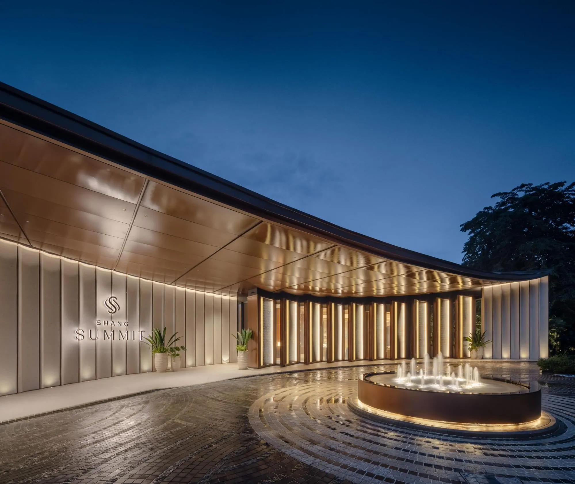 Shang Summit entrance at night with warm lighting, landscaped surroundings, and an illuminated fountain